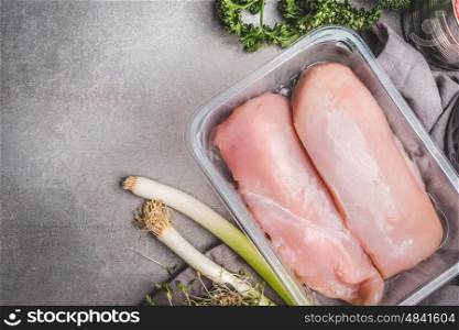 Raw chicken breast fillet in plastic box with green seasoning on concrete background, top view, place for text