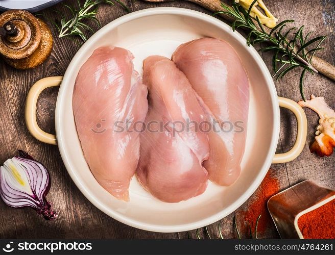Raw chicken breast in round enamelled casserole with herbs and spices, prearation, top view