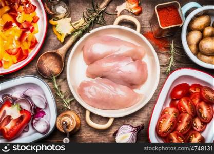Raw chicken breasts , colorful cut vegetables in bowls , flavoring and cooking spoon. Preparation on rustic wooden background, top view