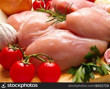 Raw chicken breasts with vegetables on cutting board