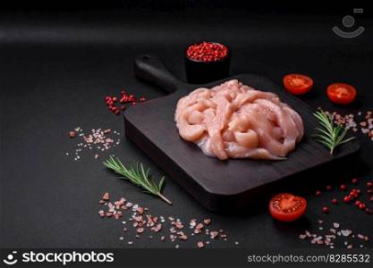 Raw chicken fillet cut into strips with spices and herbs on a wooden cutting board