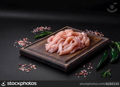 Raw chicken fillet cut into strips with spices and herbs on a wooden cutting board