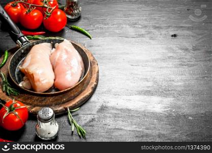 Raw chicken fillet with tomatoes and herbs. On the black chalkboard.. Raw chicken fillet with tomatoes and herbs.
