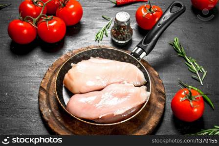 Raw chicken fillet with tomatoes and herbs. On the black chalkboard.. Raw chicken fillet with tomatoes and herbs.