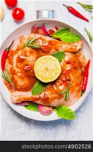 raw chicken legs whith red spicy sauce, preparation in white frying pan, top view, close up