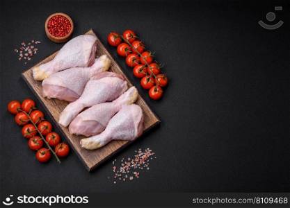 Raw chicken legs with salt, spices and herbs on a dark concrete background