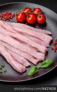 Raw chicken or turkey fillet cut into strips with spices and herbs on a dark concrete background