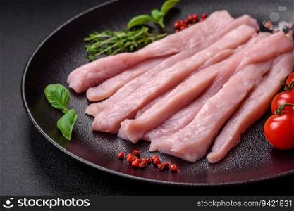 Raw chicken or turkey fillet cut into strips with spices and herbs on a dark concrete background