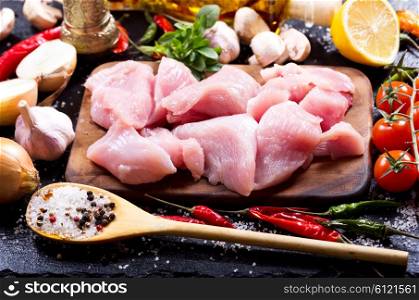 Raw chicken pieces with vegetables on dark board