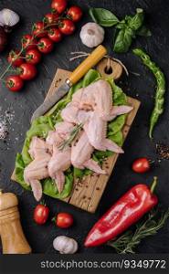 Raw chicken wings with ingredients for cooking on a wooden cutting board over dark stone background