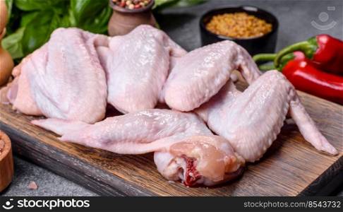 Raw chicken wings with ingredients for cooking on a wooden cutting board over gray slate. Raw chicken wings with ingredients for cooking on a wooden cutting board