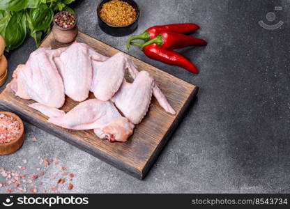 Raw chicken wings with ingredients for cooking on a wooden cutting board over gray slate. Raw chicken wings with ingredients for cooking on a wooden cutting board