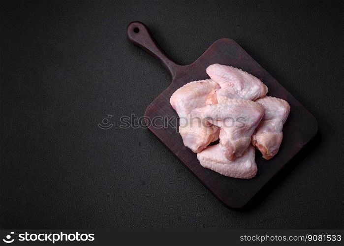 Raw chicken wings with salt, spices and herbs on a wooden cutting board on a dark concrete background