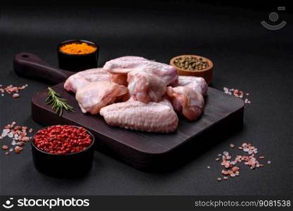Raw chicken wings with salt, spices and herbs on a wooden cutting board on a dark concrete background