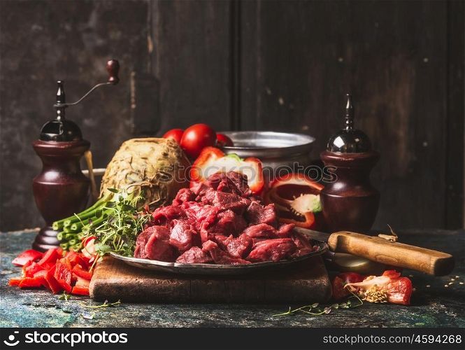 Raw chopped Beef goulash of young bulls with vegetables and cooking ingredients on dark rustic kitchen table , preparation.