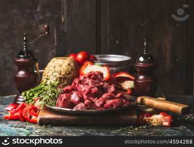 Raw chopped Beef goulash of young bulls with vegetables and cooking ingredients on dark rustic kitchen table , preparation.