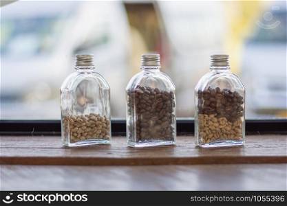 Raw coffee beans in bottles on a wooden table with indoor lighting