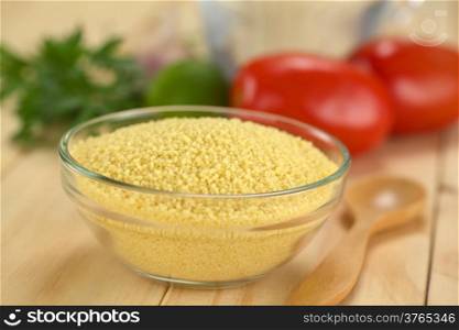 Raw couscous in glass bowl with ingredients in the back (Selective Focus, Focus one third into the couscous)