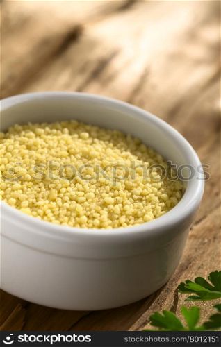 Raw couscous in small bowl on wood photographed with natural light (Selective Focus, Focus one third into the couscous)