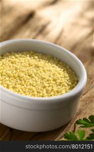 Raw couscous in small bowl on wood photographed with natural light (Selective Focus, Focus one third into the couscous)