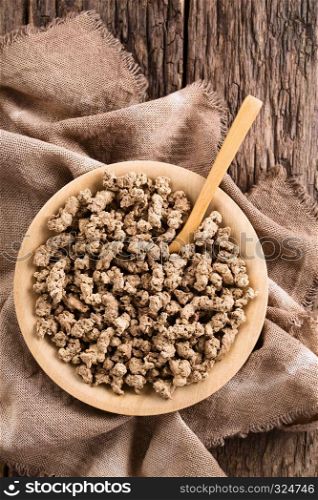 Raw dehydrated soy meat, soy protein, soya chunks or textured vegetable protein on wooden plate with spoon, photographed overhead on rustic wood. Raw Dehydrated Soy Meat