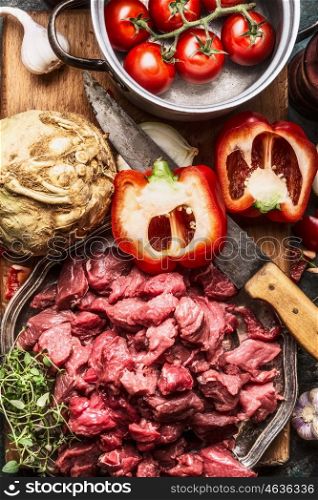 Raw diced beef meat , vegetables ingredient , kitchen knife and cooking pot . Stew or goulash preparation, top view