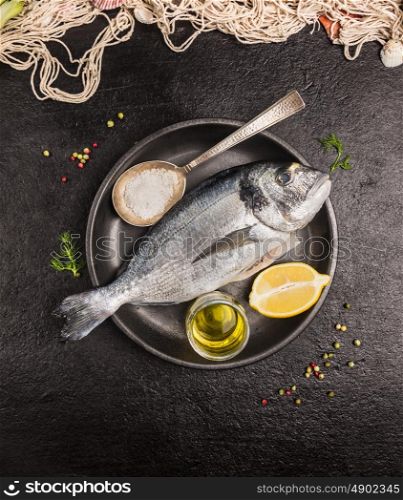 Raw dorado fish in gray rustic plate with lemon,oil and spoon of salt on dark stone background, top view
