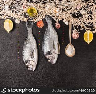 Raw dorado fish with spoon of salt,lemon,spices and fishing net on black stone background, top view