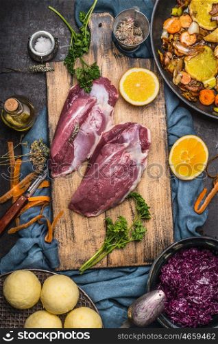 Raw Duck breast with ingredients for tasty cooking: oranges,vegetables, dumpling and red cabbage on cutting board at dark rustic kitchen table, top view. German cuisine concept