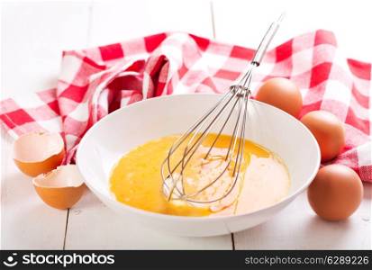 raw eggs with whisk in bowl on wooden table