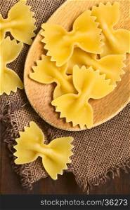 Raw farfalle or bow-tie pasta on wooden spoon, photographed overhead with natural light (Selective Focus, Focus on the pasta on the spoon)