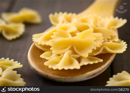 Raw farfalle or bow-tie pasta on wooden spoon, photographed with natural light (Selective Focus, Focus on the middle of the upper pasta on the spoon)