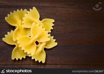 Raw farfalle or bow-tie pasta, photographed overhead on dark wood with natural light (Selective Focus, Focus on the top pasta)
