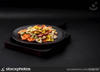 Raw farfalle pasta in different colors on a dark concrete background. Preparing to cook Italian food