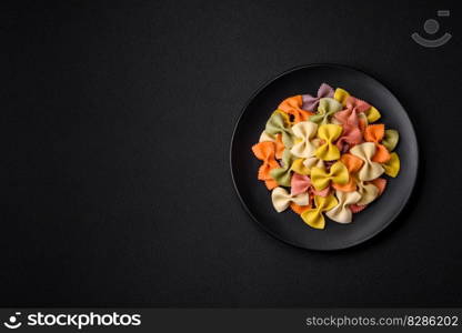 Raw farfalle pasta in different colors on a dark concrete background. Preparing to cook Italian food