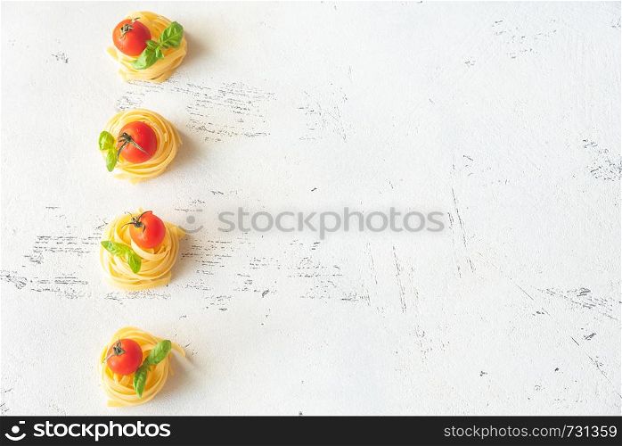 Raw fettuccine with cherry tomatoes and fresh basil leaves on the white background