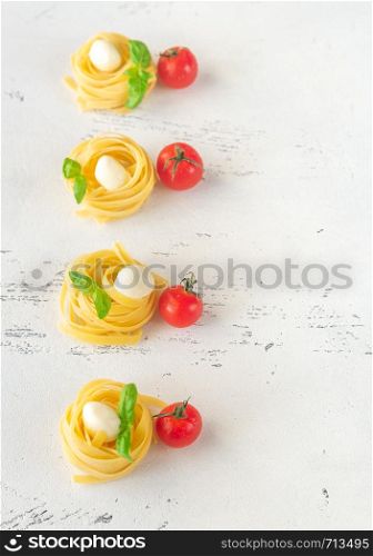 Raw fettuccine with mozzarella balls, cherry tomatoes and fresh basil leaves on the white background