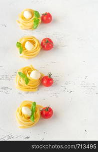 Raw fettuccine with mozzarella balls, cherry tomatoes and fresh basil leaves on the white background