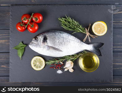 Raw fish dorado cooking and ingredients. Dorado, lemon, tomato, herbs and spices. Top view on wood table