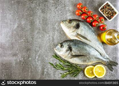 Raw fish dorado on grey concrete background with sπces, tomato, rosemary, olive oil and≤mon. Top view, flat lay with©space for text. Fresh fish dorado on grey concrete background with ingredients for cooking