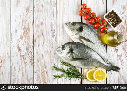 Raw fish dorado on white wooden background with spices, tomato, rosemary, olive oil and lemon. Top view, flat lay with copy space for text. Fresh fish dorado on white wooden background with ingredients for cooking