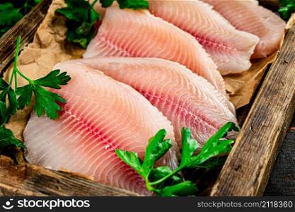 Raw fish fillet on a wooden tray with parsley. Against a dark background. High quality photo. Raw fish fillet on a wooden tray with parsley.