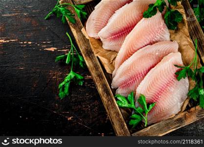 Raw fish fillet on a wooden tray with parsley. Against a dark background. High quality photo. Raw fish fillet on a wooden tray with parsley.
