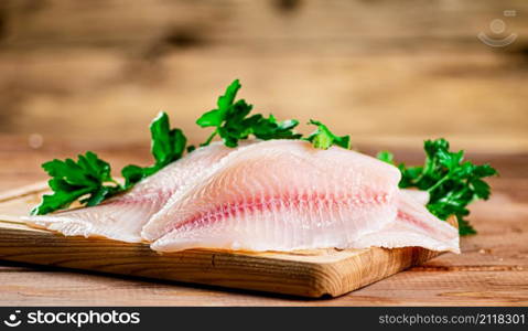 Raw fish fillet with parsley on a cutting board. On a wooden background. High quality photo. Raw fish fillet with parsley on a cutting board.