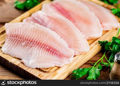 Raw fish fillet with parsley on a cutting board. On a wooden background. High quality photo. Raw fish fillet with parsley on a cutting board.