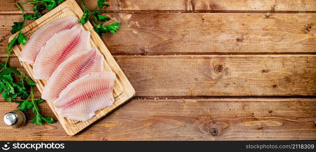 Raw fish fillet with parsley on a cutting board. On a wooden background. High quality photo. Raw fish fillet with parsley on a cutting board.