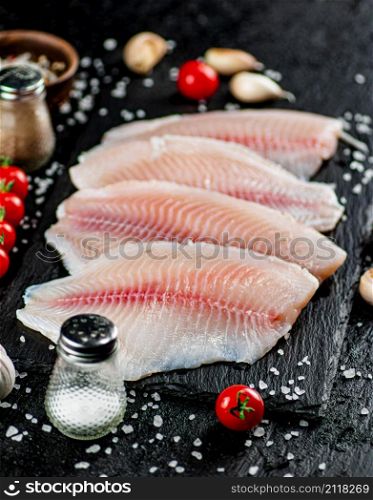 Raw fish fillet with spices and tomatoes on a stone board. On a black background. High quality photo. Raw fish fillet with spices and tomatoes on a stone board.