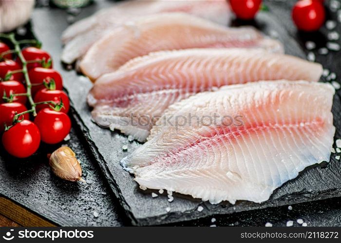 Raw fish fillet with spices and tomatoes on a stone board. On a black background. High quality photo. Raw fish fillet with spices and tomatoes on a stone board.