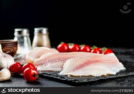 Raw fish fillet with tomatoes and spices. On a black background. High quality photo. Raw fish fillet with tomatoes and spices.