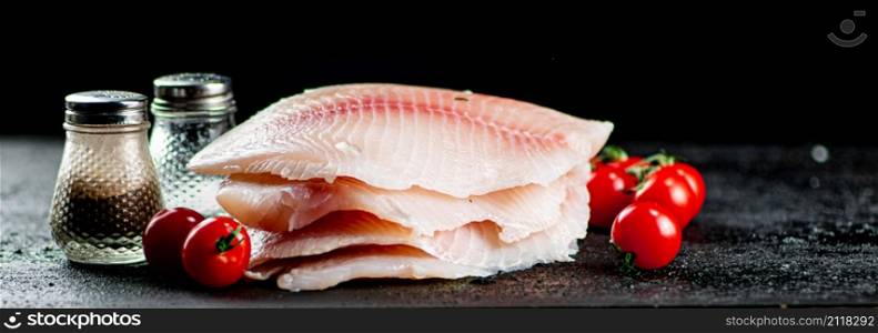 Raw fish fillet with tomatoes and spices. On a black background. High quality photo. Raw fish fillet with tomatoes and spices.